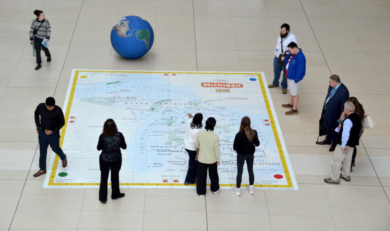 Attendees explore a giant map of Michigan displayed in the Huntington Center atrium during AAG 2025 in Detroit