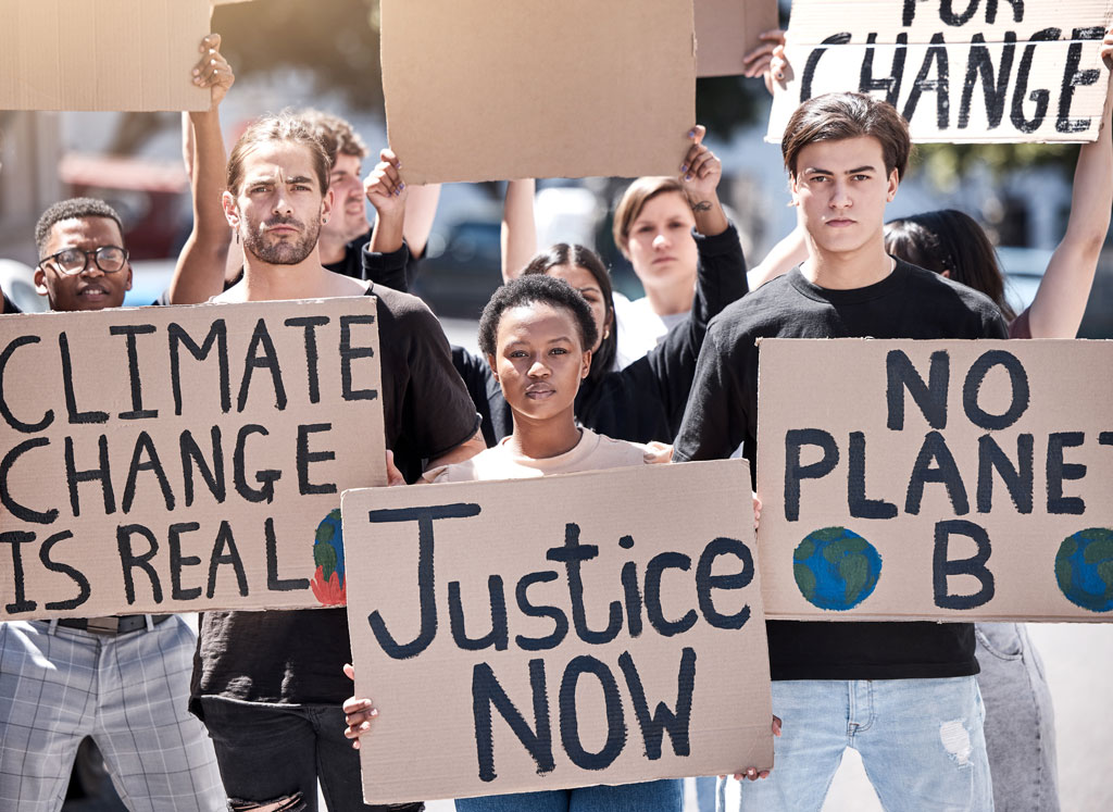 A diverse group of protesters hold cardboard signs in support of environmental justice